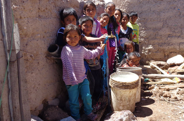 Latin American children stand in a line filling buckets with water