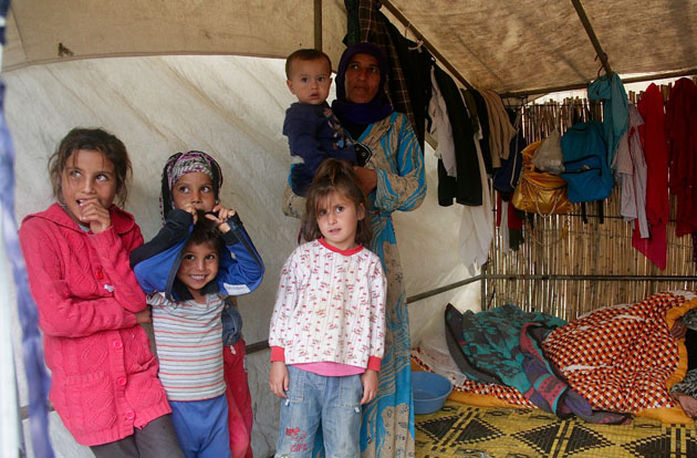 Middle Eastern mother and children stand in their home made of canvas