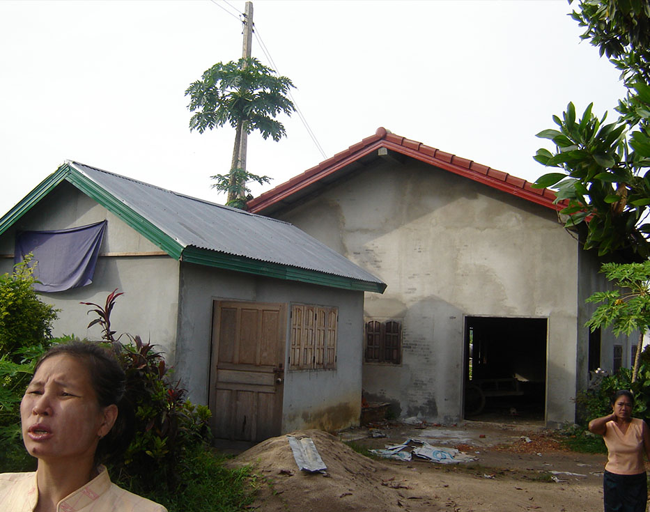 Two Lao women stand outside of their house with concerned faces