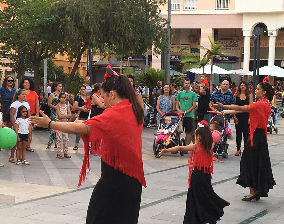 Spanish women and girls wearing red and black dresses dancing for an audience in a public area