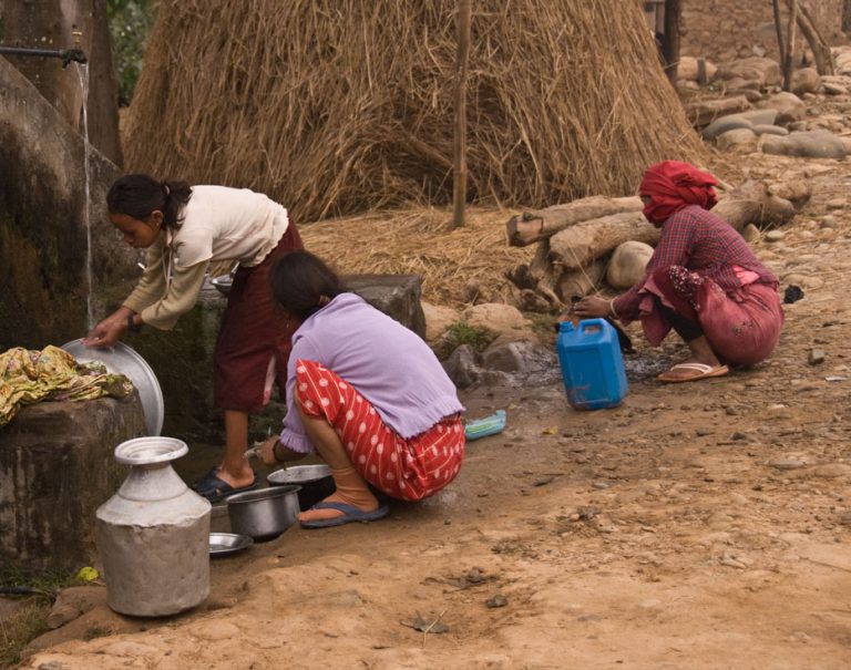 Nepalese women wash cookware with water from communal water pump