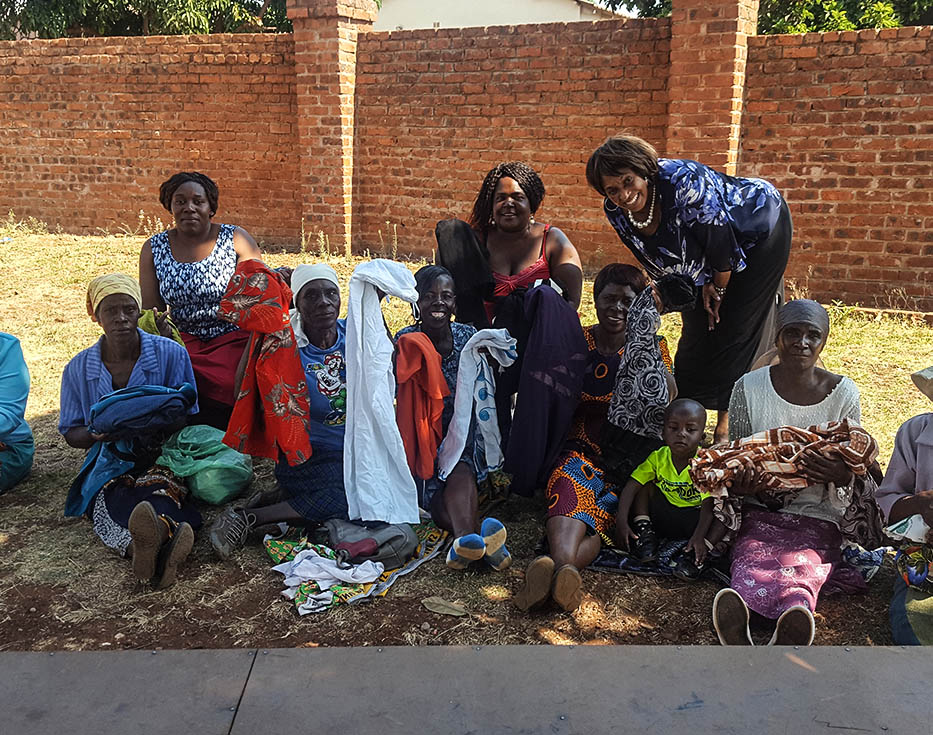 Zimbabwean women sitting on the ground holding clothes in their hands with a brick wall behind them