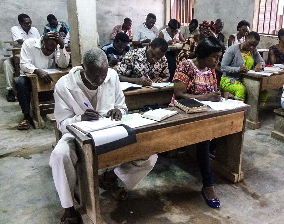 Cameroonian men and women sitting at desks in a classroom completing an assignment