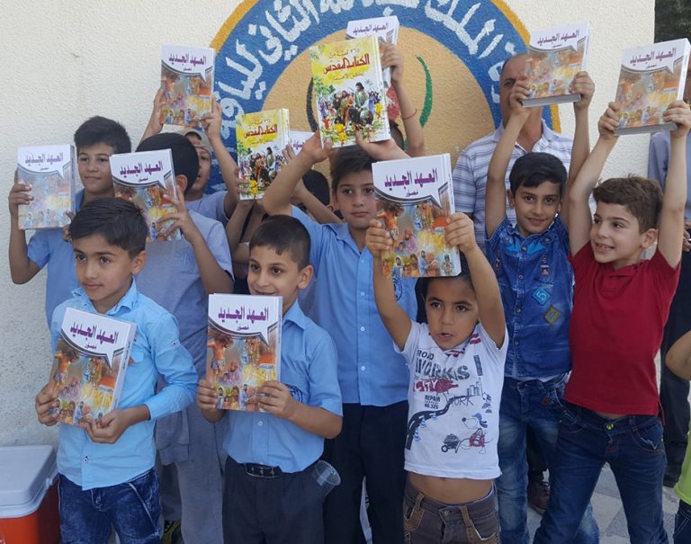 Jordanian boys stand in front of a wall holding up their children's bibles translated into Arabic