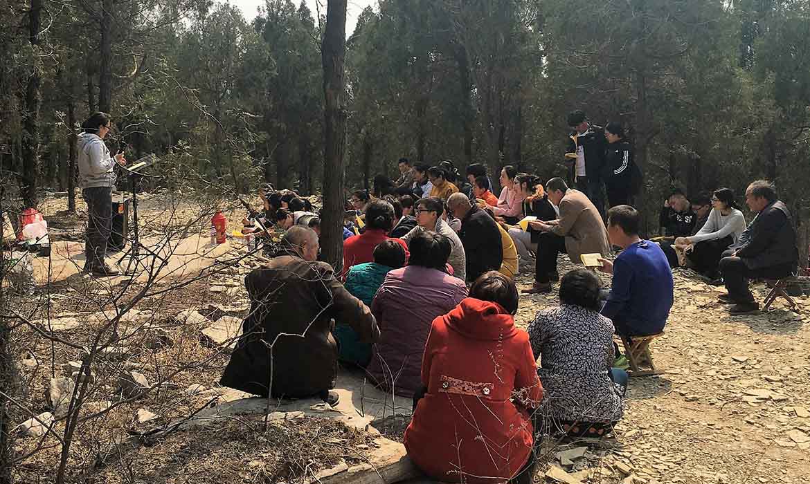 Chinese Christians sit in a group in a forest listening to a Christian leader speak