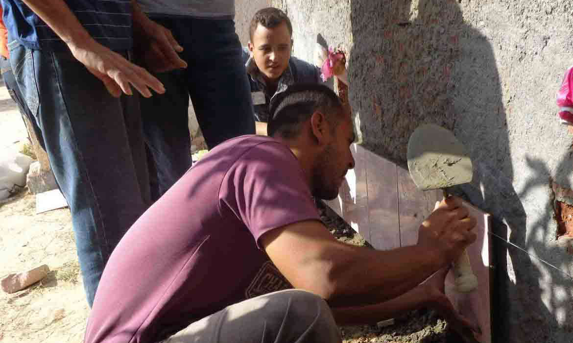 A Christian Egyptian man places tile on a wall layered with cement while others watch