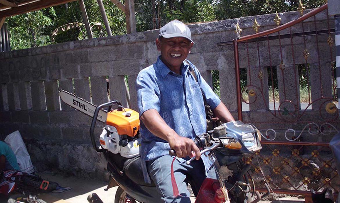 Indonesian man smiling while sitting on his motorcycle with his chainsaw on the back