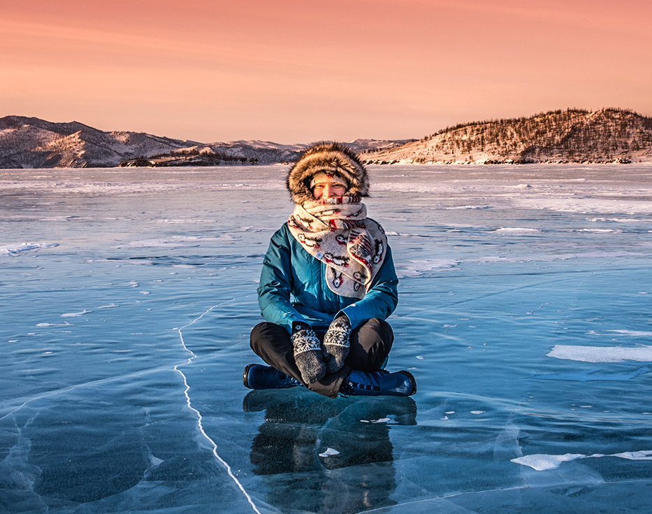 Russian woman dressed in warm winter clothes sitting on a frozen lake