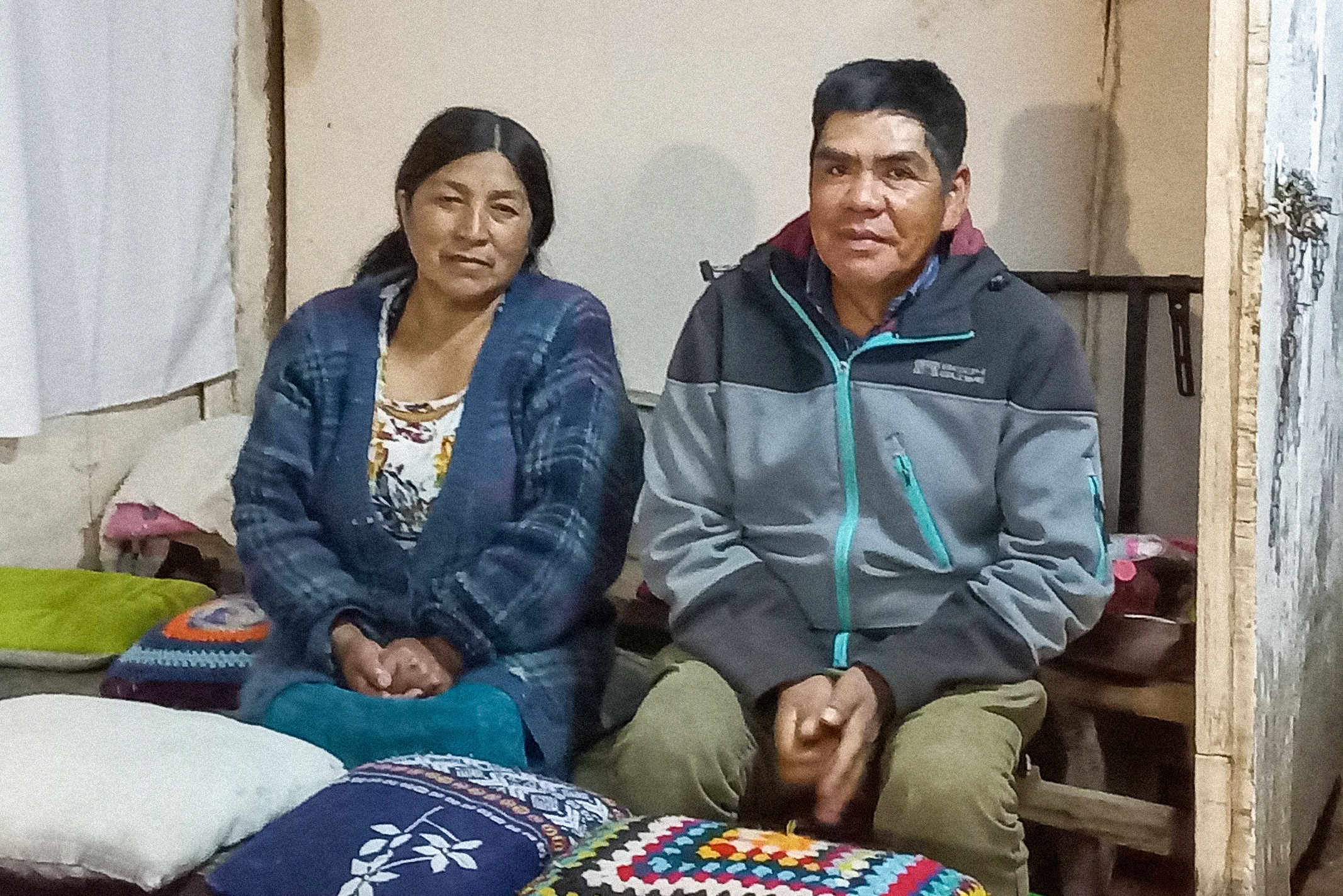 A man and woman sitting on a bench in their house in Chile wearing jackets