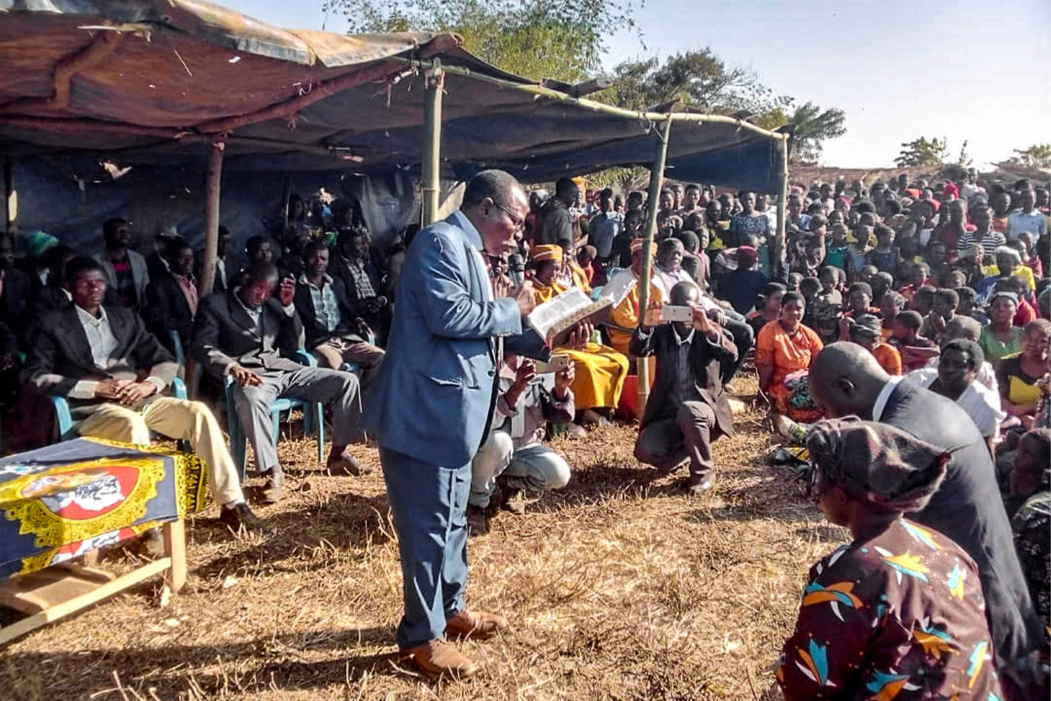 A Christian chief of a village in Africa reads from the Bible to an audience gathered around him for his inaugural ceremony