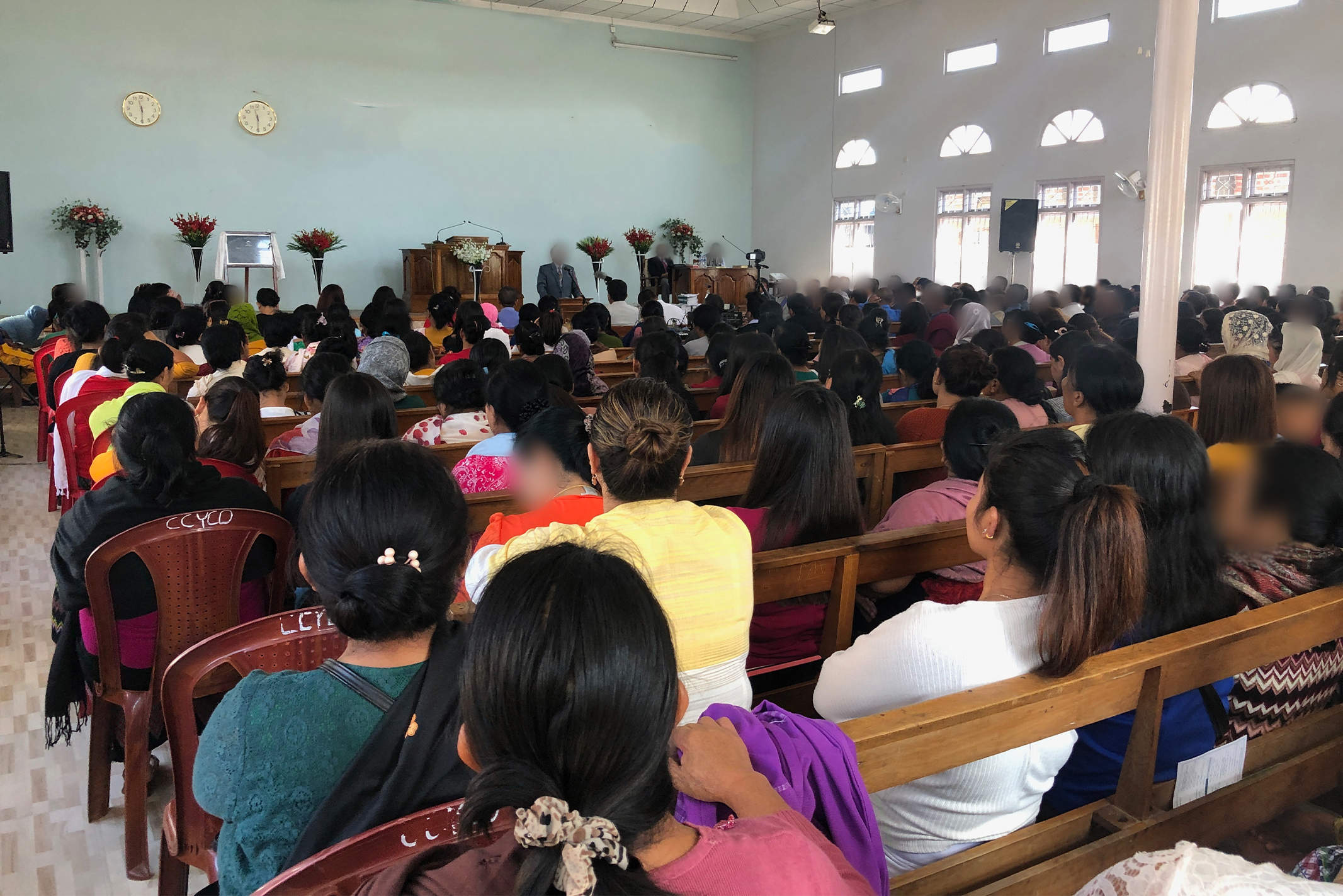 Christians in South Asia gather in their church for service sitting on wooden pews looking at their pastor preaching